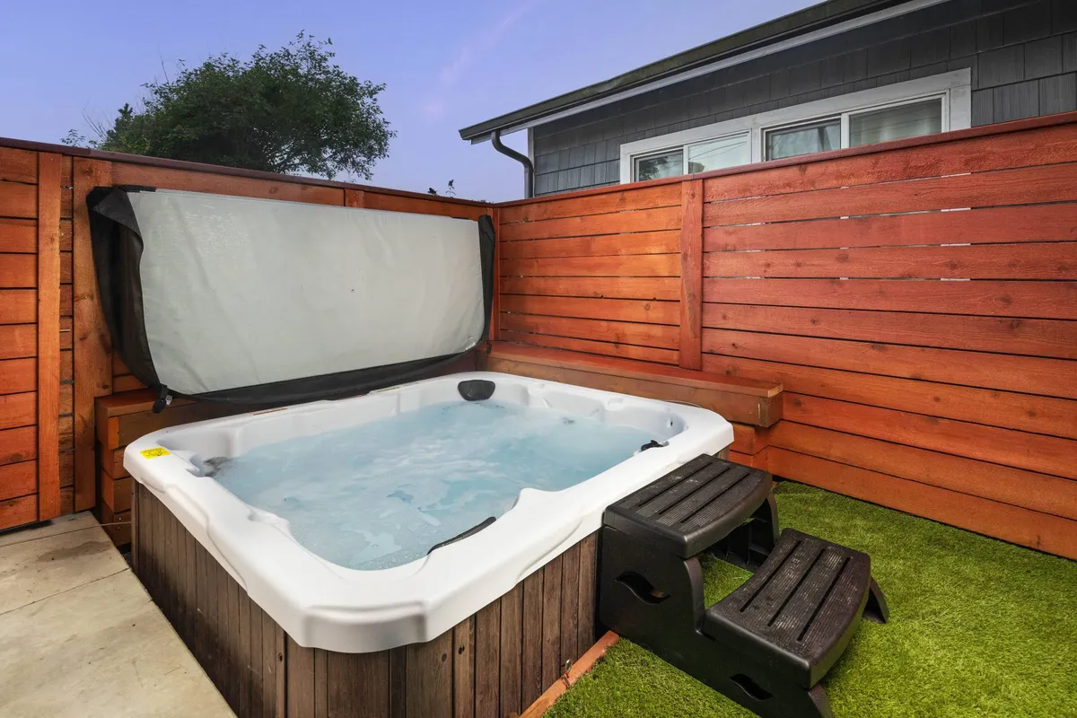 An inviting outdoor hot tub set in a grassy yard, bordered by wooden fencing for privacy. The area has plenty of space for relaxing or socializing, and the hot tub is positioned to enjoy the fresh air and views.