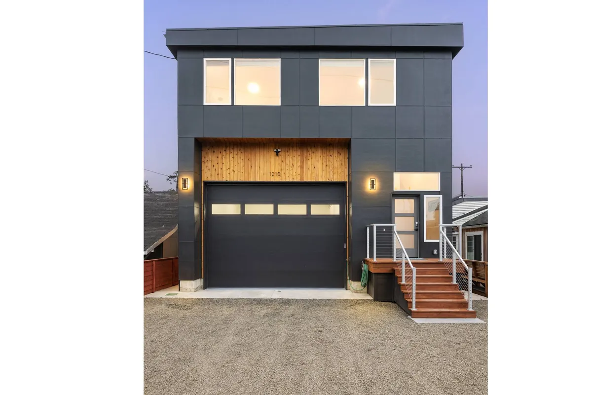 The hero image showcases a modern single-family house with striking wooden accents, expansive windows, and a set of inviting stairs leading up to the entrance. The design is both contemporary and warm, suggesting a perfect blend of comfort and style. The spacious porch hints at opportunities for sunset viewing, family gatherings, and outdoor entertaining, all set just steps from both the lake and the beach.