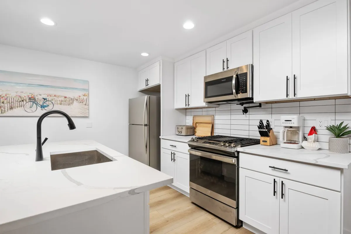 A bright, modern kitchen featuring sleek appliances, white cabinetry, and inviting decor. The kitchen's spacious layout is ideal for preparing meals together or casual conversations during breaks. Decorative wall art and thoughtful organization contribute to a vibrant, yet purposeful, atmosphere.