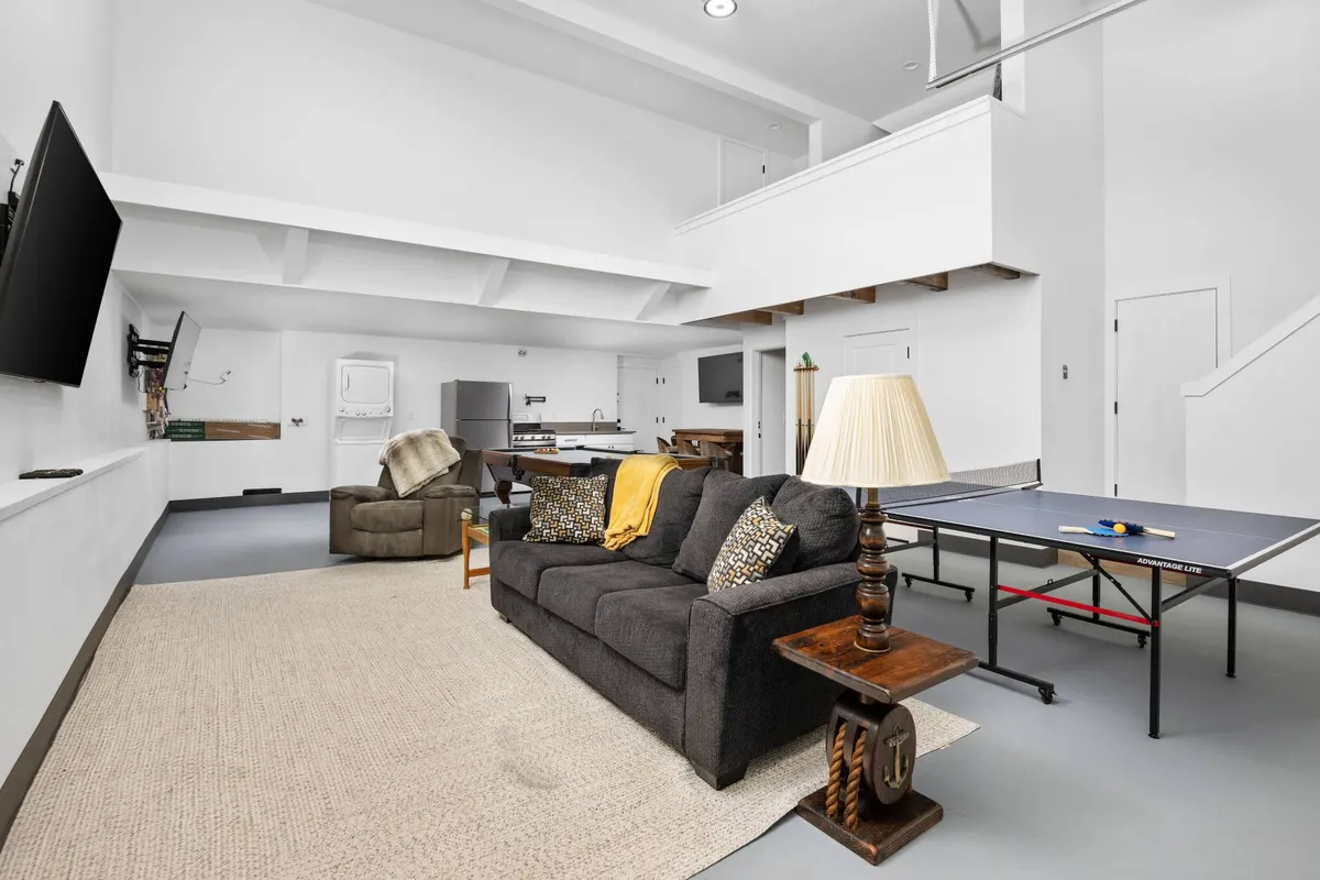 A cozy corner of the game room with a plush sofa and a ping pong table in view. Warm lighting and casual decor set the tone for relaxed gatherings, ideal for friendly games or unwinding with family and friends.