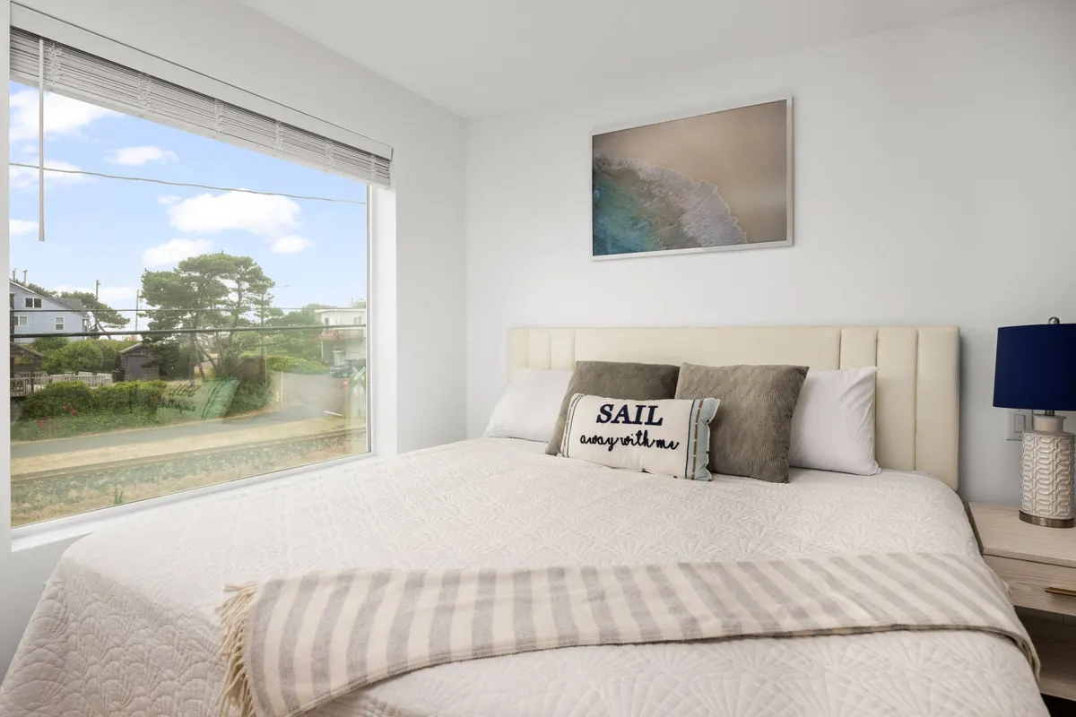 A relaxing queen bedroom featuring a bed with decorative pillows, a large window providing a pleasant view and natural light, and soothing wall art. The room feels restful and welcoming—ideal for guests seeking privacy and comfort.