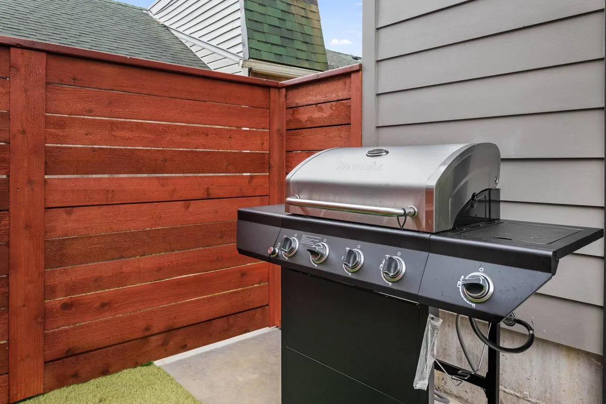 A relaxed outdoor area with a grill, green grass, and a wooden fence—ideal for barbecuing, outdoor dining, and spending time with loved ones (including pets).