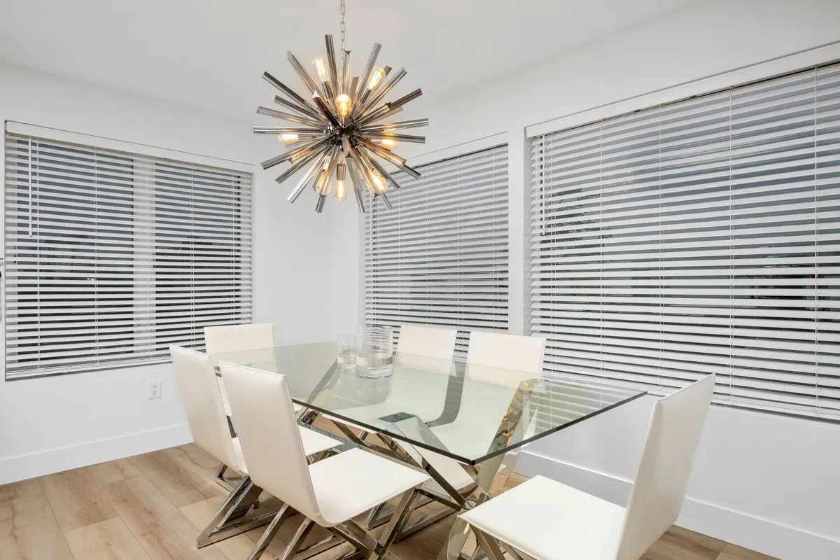 A stylish dining area with a glass table, white chairs, and a statement chandelier. The ample natural light and contemporary furnishings create a setting that encourages group interaction, whether for working sessions, team meals, or socializing after hours.