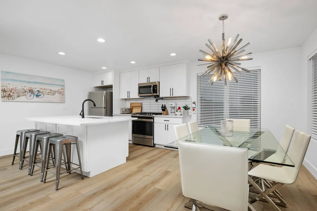 A bright, contemporary kitchen and dining area featuring an island bar with stools, a glass dining table, and modern lighting. The room exudes a cheerful atmosphere perfect for socializing, sharing meals, and planning the day’s pet-friendly excursions.