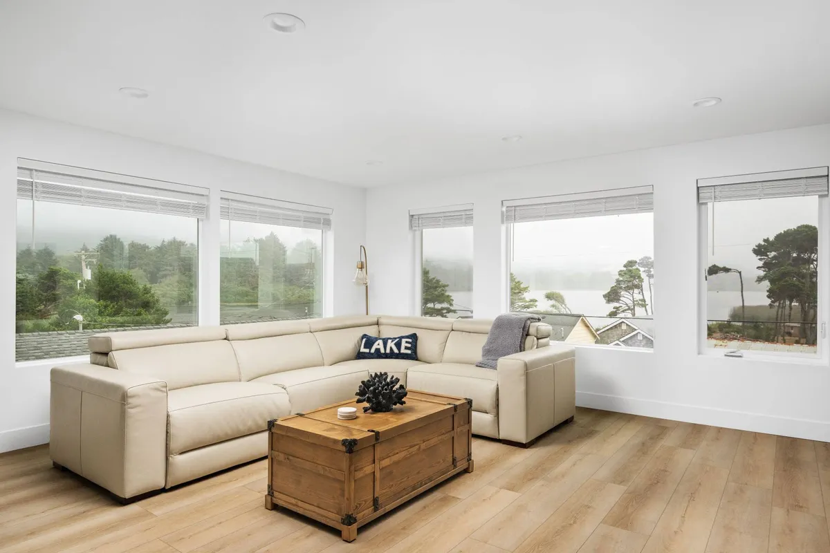 Another angle on a living area with a sectional sofa and wooden coffee table, again featuring expansive windows that flood the room with natural light and provide serene views of the lake. The arrangement is conducive to both intimate family gatherings and quiet moments.
